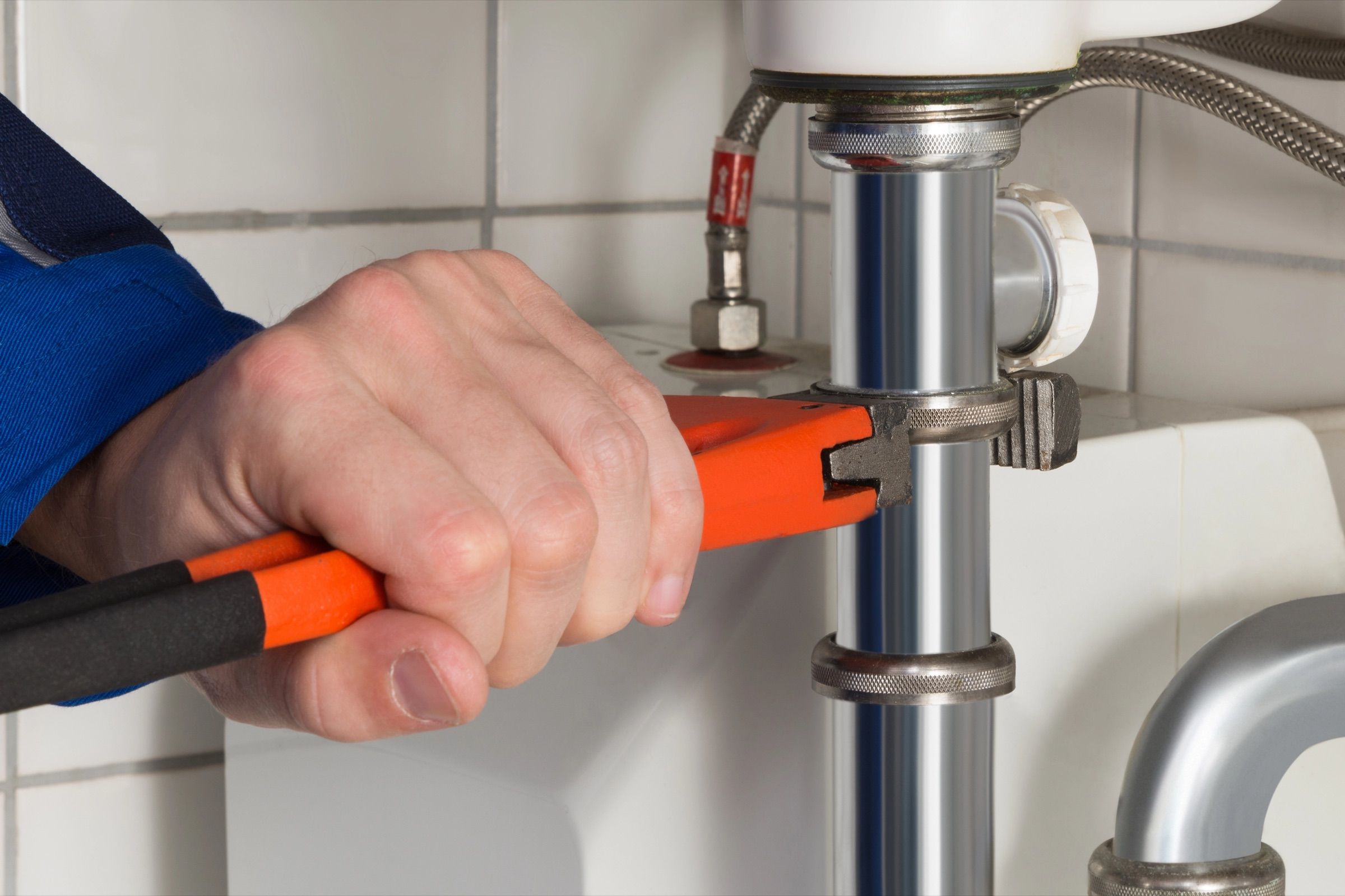 Plombier qui resserre un raccord de siphon sous un lavabo